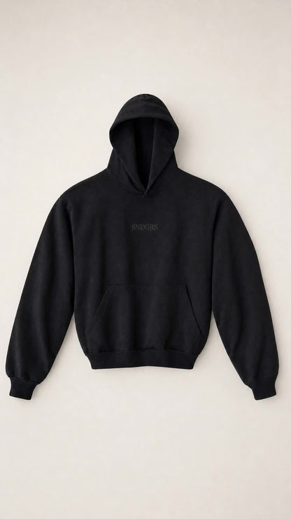 Front view of the SNDGRS STILL. Volume 001 black heavyweight pullover on an off-white background.