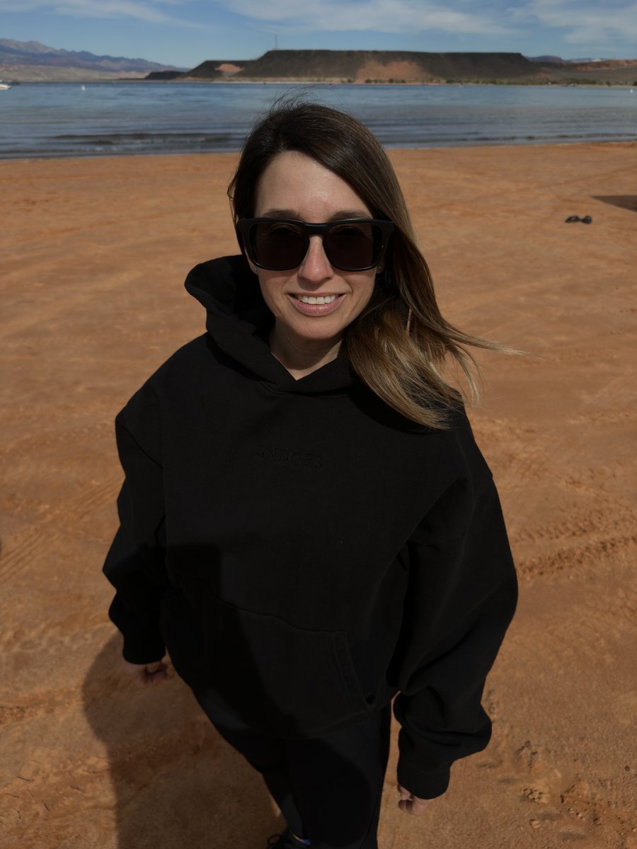 A wearer in a black SNDGRS hoodie on the red shore at Sand Hollow.